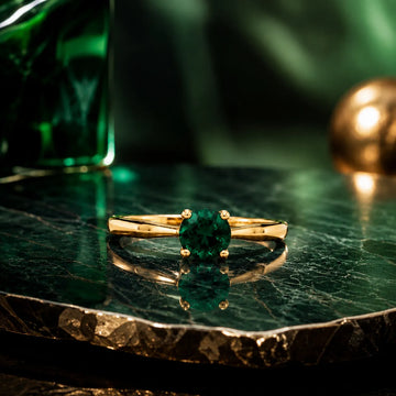 Gold ring with a green gemstone on a reflective surface