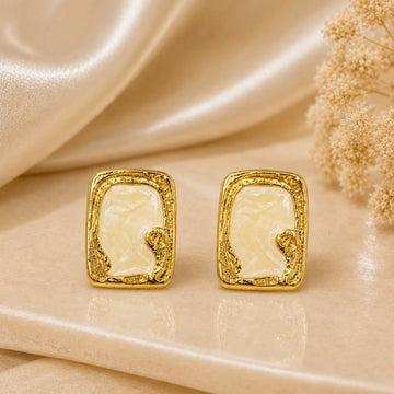 Gold earrings with a white center on a beige fabric background