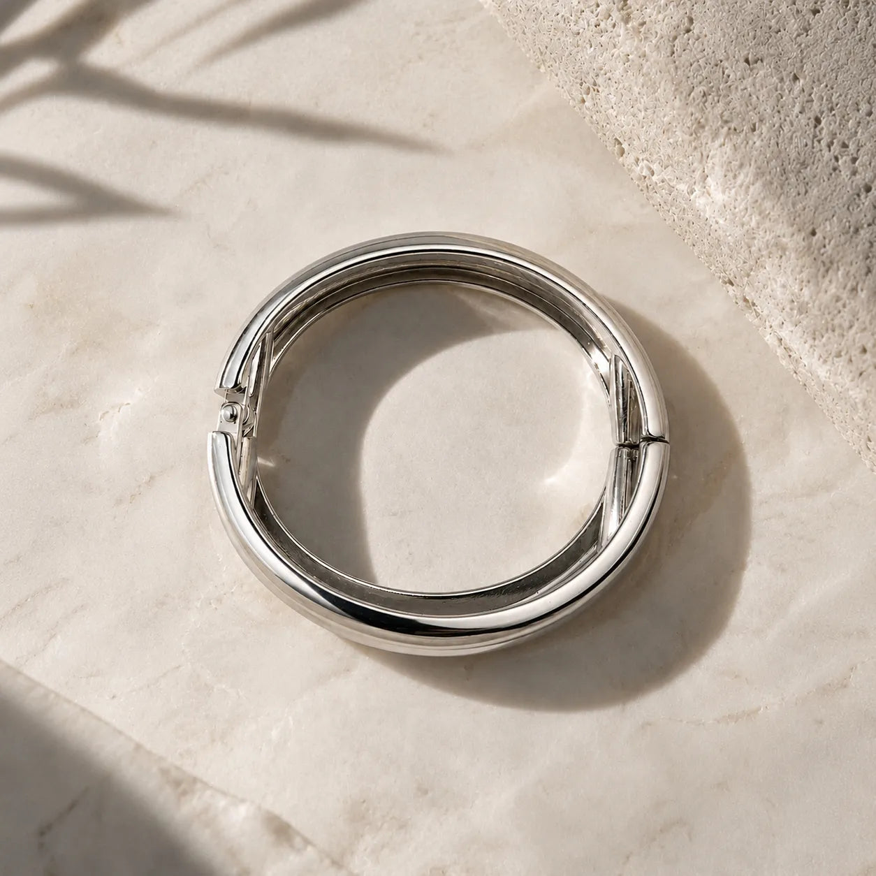 Silver ring on a light stone surface with natural light and shadow