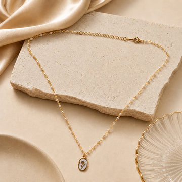Gold necklace with a pendant on a beige stone surface