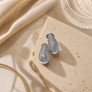 Silver earrings on a textured beige surface with soft lighting