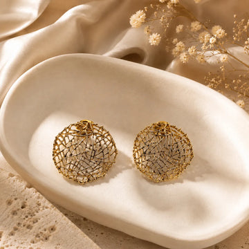 Gold earrings on a textured beige surface with dried flowers in the background