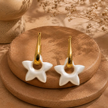 Gold and white star-shaped earrings on a brown surface with dried flowers in the background.
