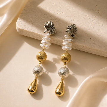 Pair of gold and silver earrings on a beige stone surface