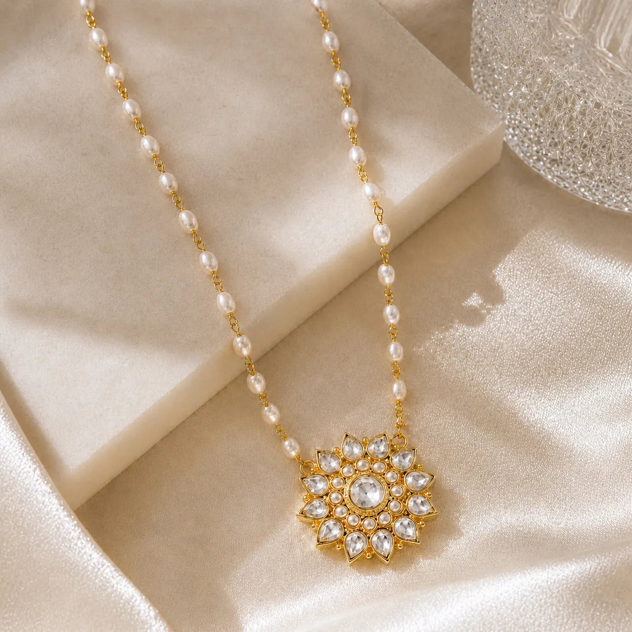Pearl necklace with a gold and crystal pendant on a beige fabric background