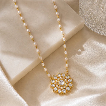 Pearl necklace with a gold and crystal pendant on a beige fabric background