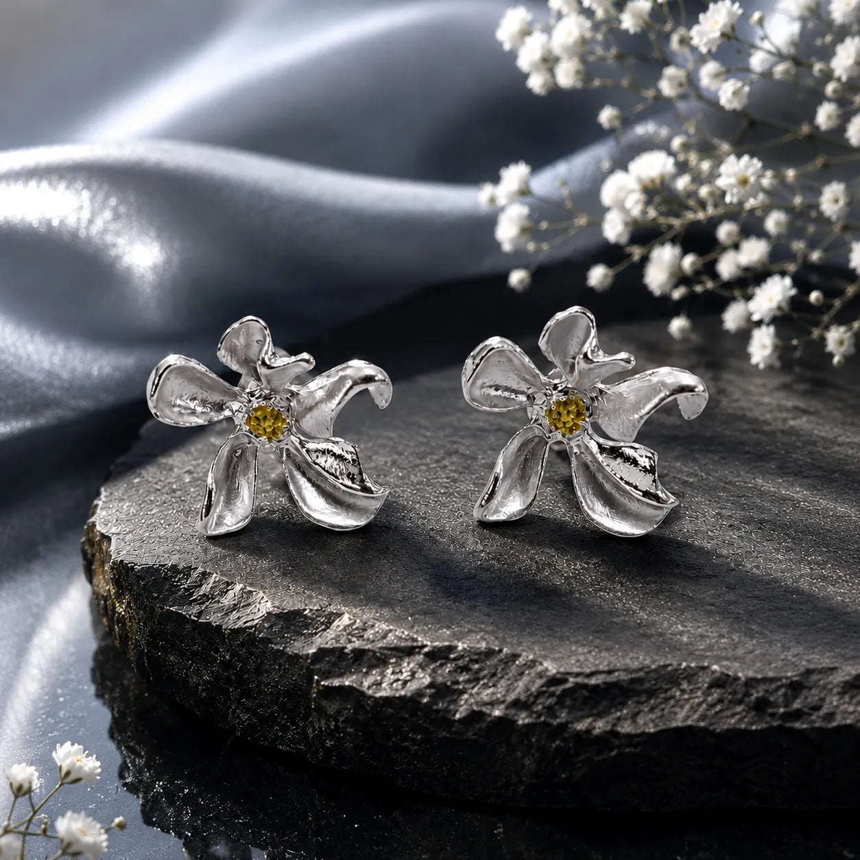 Silver flower-shaped earrings on a dark stone surface with white flowers.