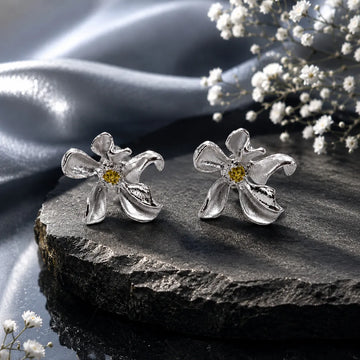 Silver flower-shaped earrings on a dark stone surface with white flowers.