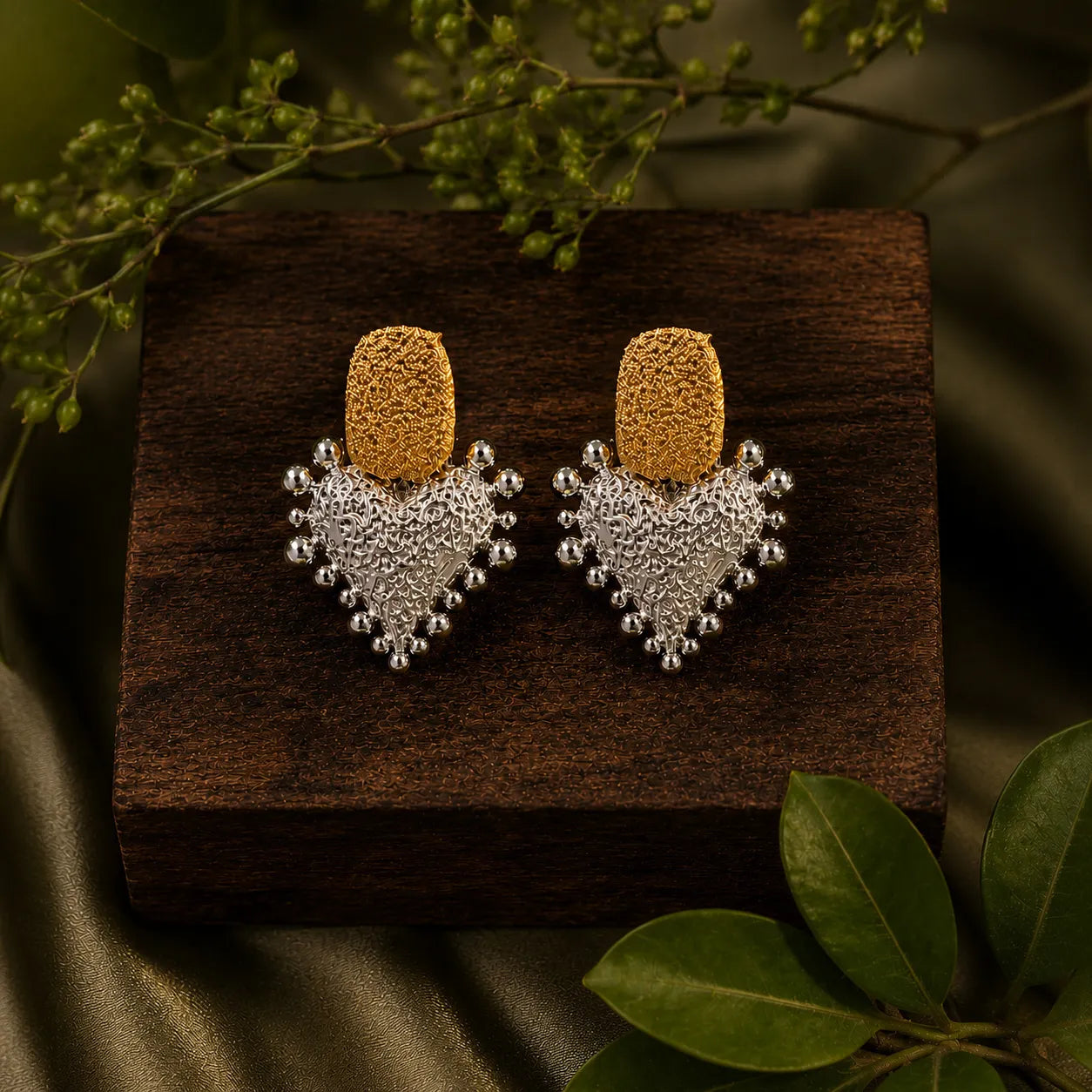 Gold and silver earrings on a wooden surface with green leaves in the background