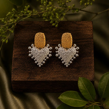 Gold and silver earrings on a wooden surface with green leaves in the background