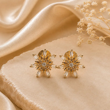 Gold earrings with clear stones on a beige fabric background