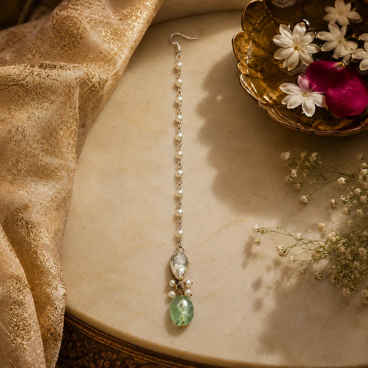 Delicate earring with green gemstone on a textured surface with flowers