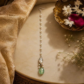 Delicate earring with green gemstone on a textured surface with flowers