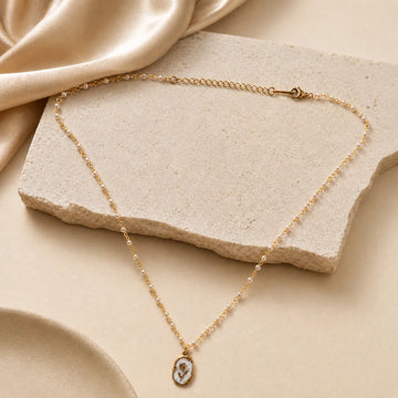 Gold necklace with a pendant on a beige stone surface