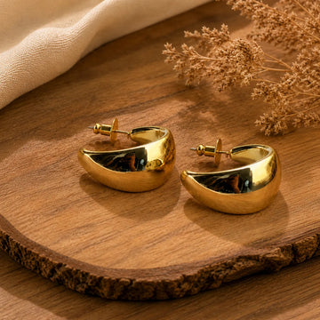 Gold hoop earrings on a wooden surface with dried flowers.