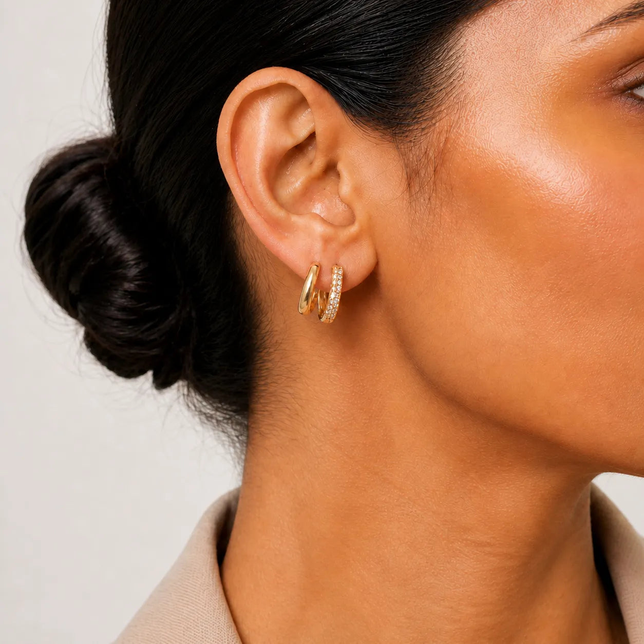 Close-up of a person wearing gold hoop earrings with a neutral background