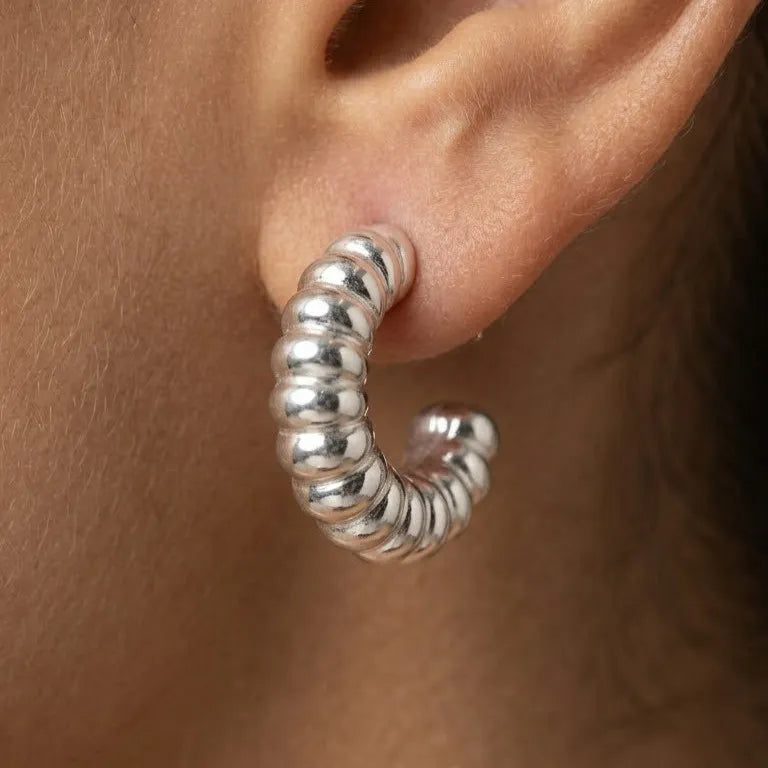 Silver hoop earring worn on an ear with a neutral background