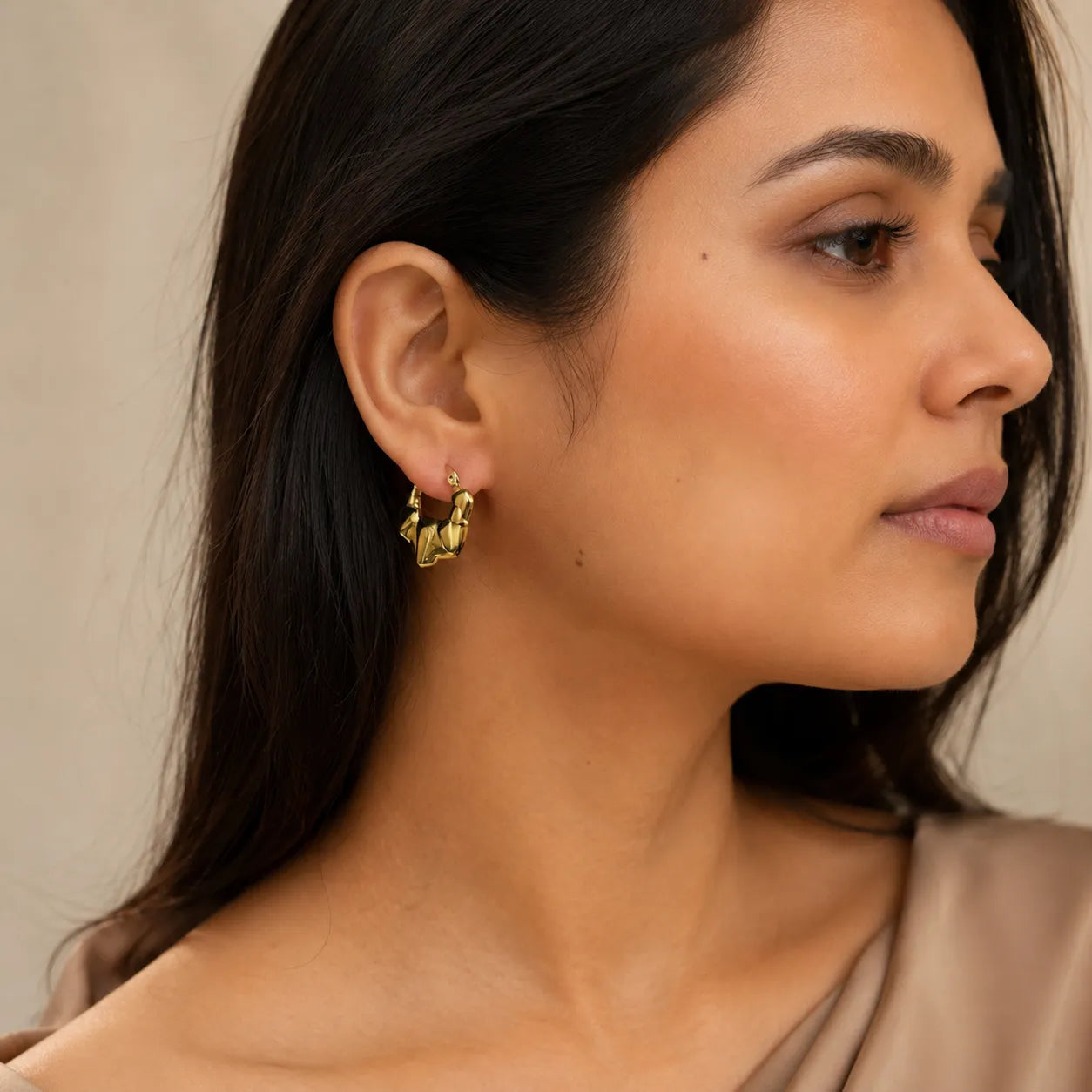 Close-up of a woman wearing gold earrings with a neutral background