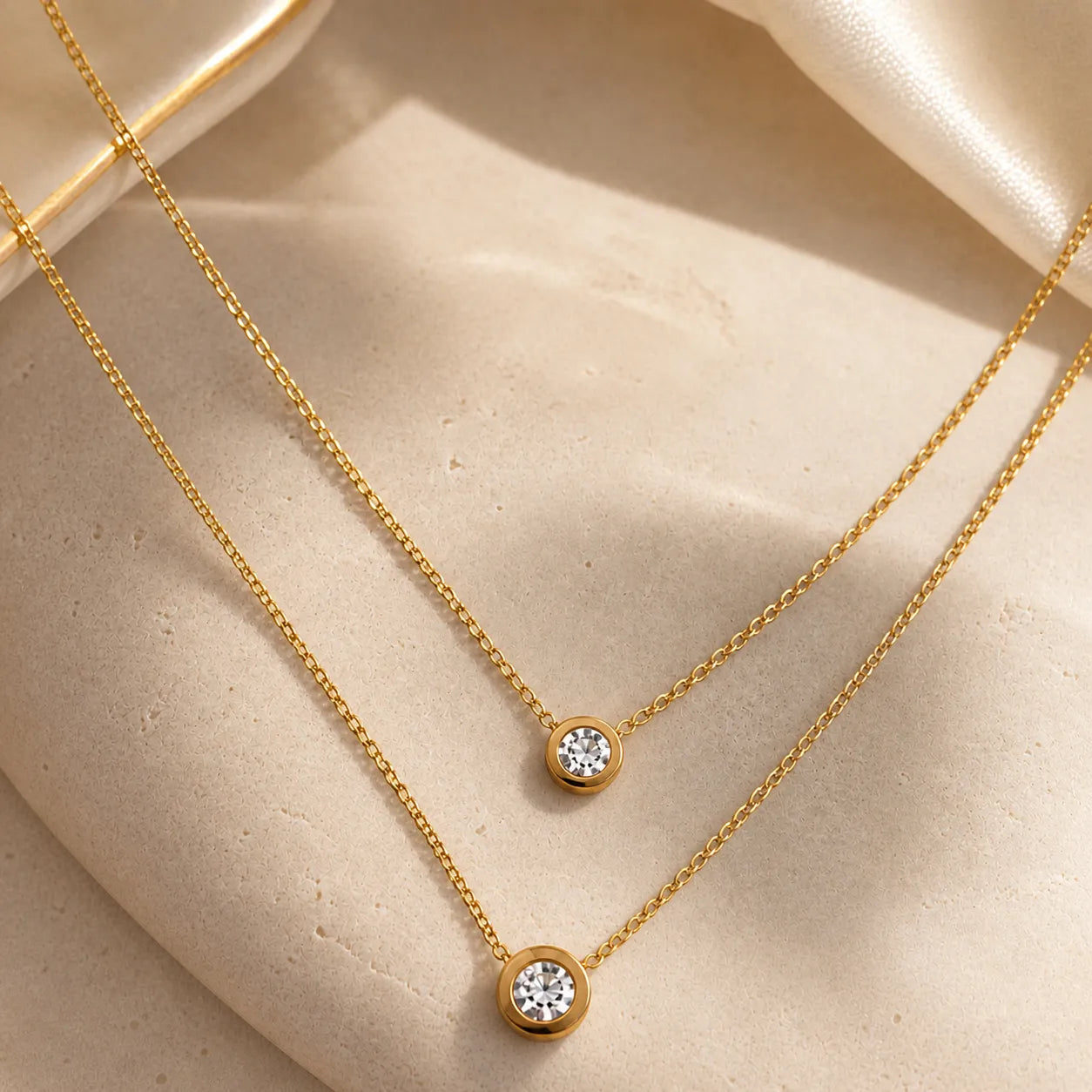 Two gold necklaces with diamond pendants on a beige surface
