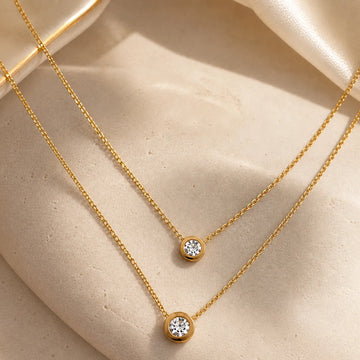 Two gold necklaces with diamond pendants on a beige surface