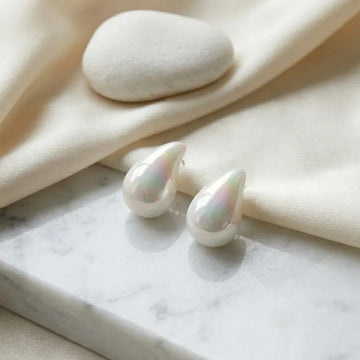Pearl earrings on a marble surface with beige fabric