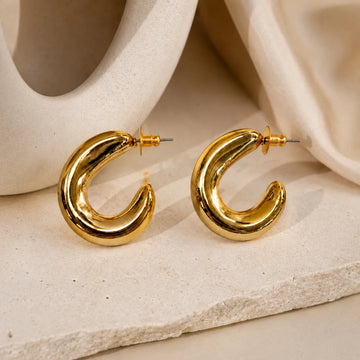 Gold hoop earrings on a textured beige surface