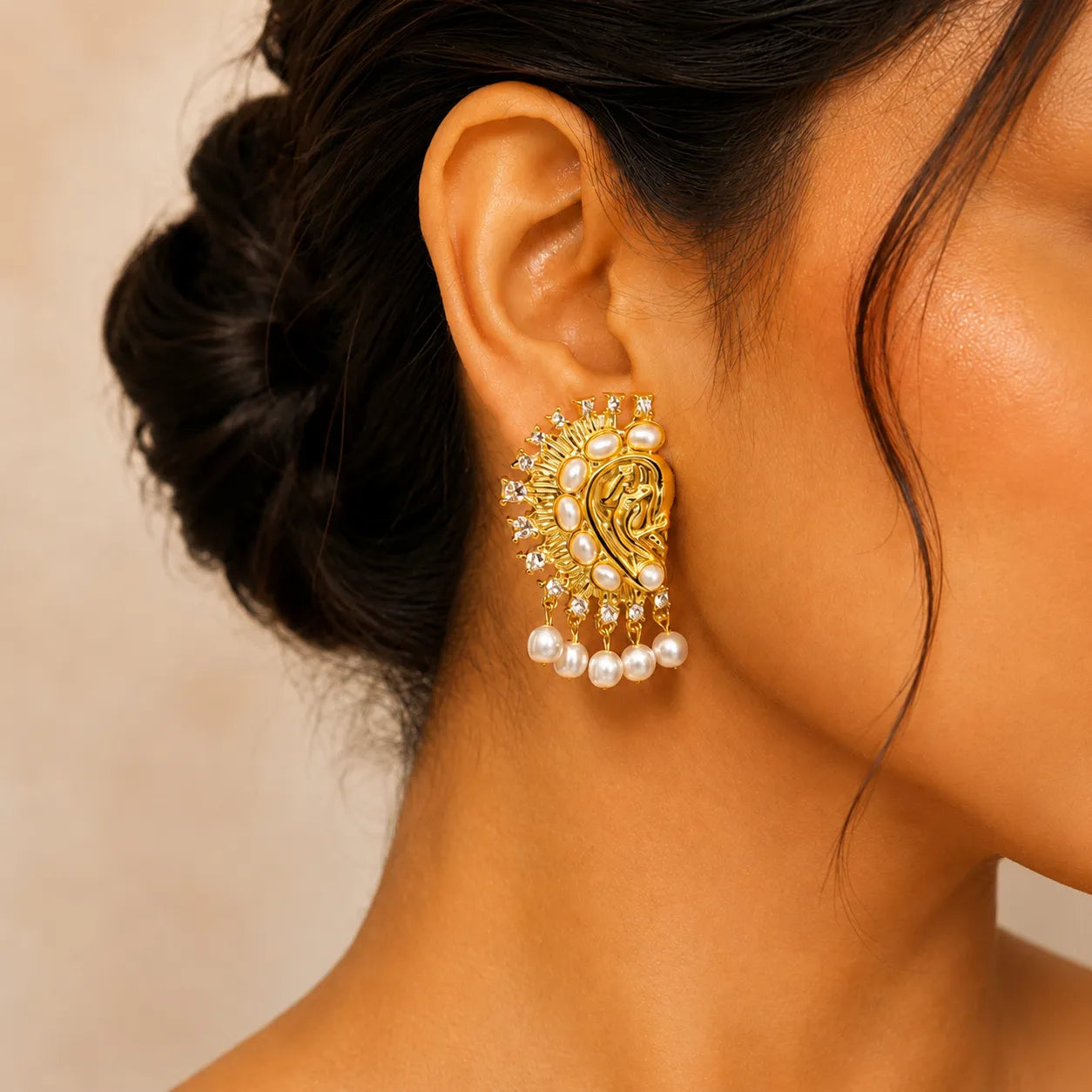 Close-up of a woman wearing a gold and pearl earring against a neutral background