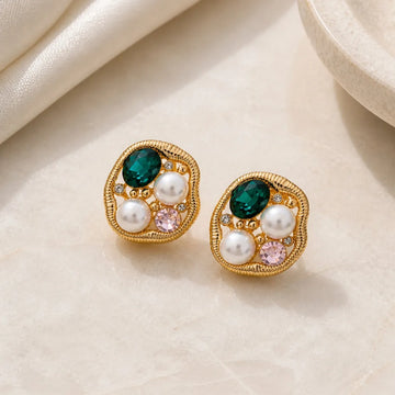 Pair of gold earrings with green, pink, and white gemstones on a beige fabric background