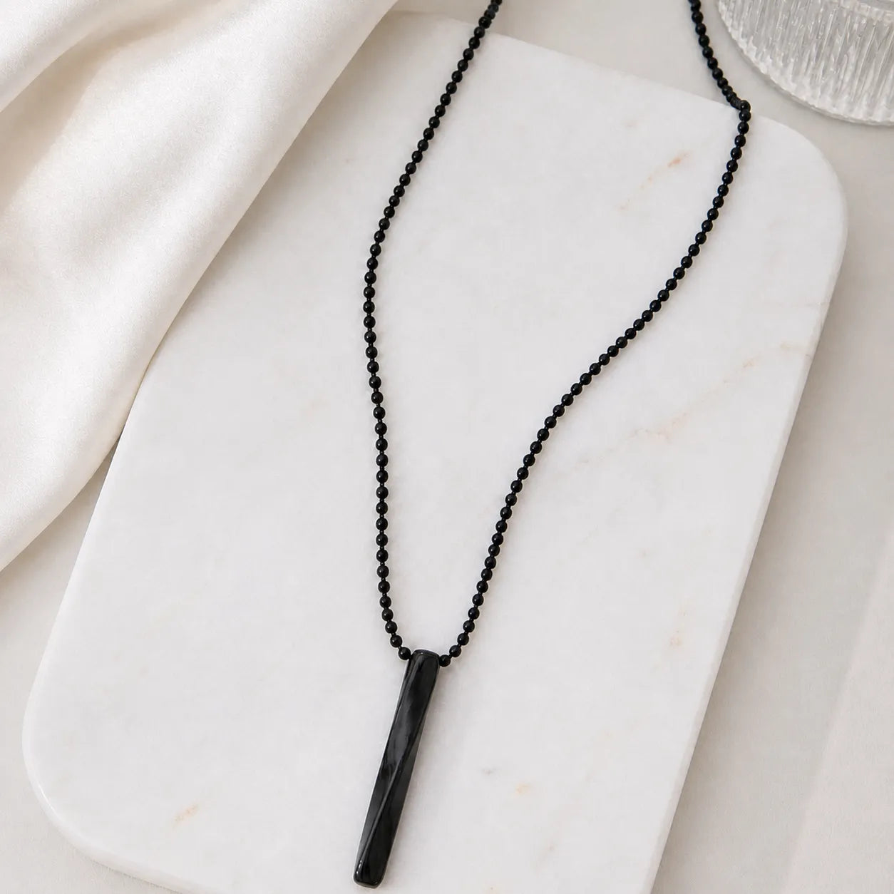 Black beaded necklace with a cylindrical pendant on a white marble surface