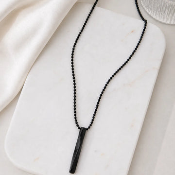 Black beaded necklace with a cylindrical pendant on a white marble surface