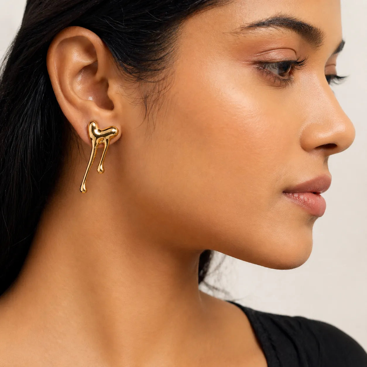 Close-up of a woman wearing gold earrings with a neutral background
