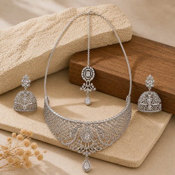 Silver necklace and earrings set on a textured surface with dried flowers.