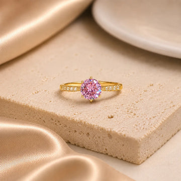 Gold ring with a pink gemstone on a beige surface