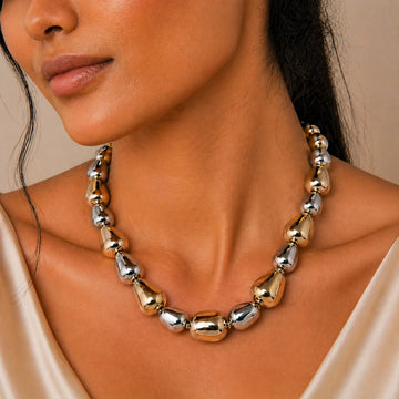 Close-up of a woman wearing a gold and silver necklace against a neutral background