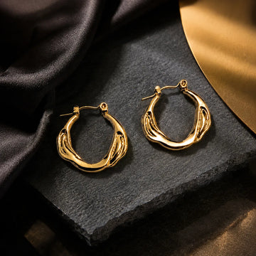 Gold hoop earrings on a dark stone surface with a gold leaf and black fabric background