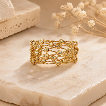 Gold ring on a textured beige surface with dried flowers in the background