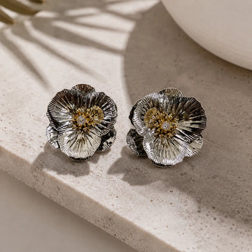 Silver floral earrings on a textured surface with soft shadows