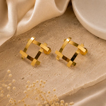 Gold geometric earrings on a beige surface with a soft fabric background