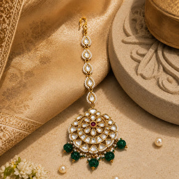 Ornate gold and green pendant with pearls on a textured beige surface
