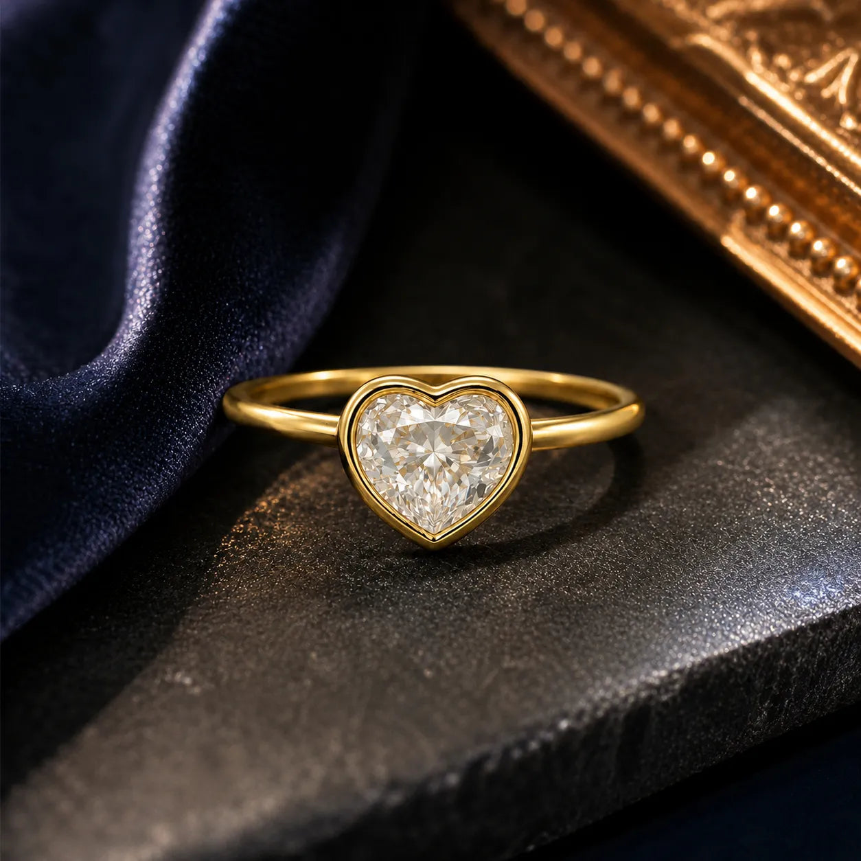 Gold heart-shaped diamond ring on a dark surface with a gold box in the background