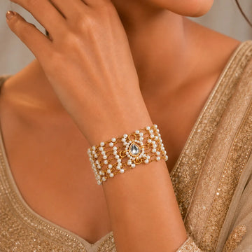 Close-up of a woman's arm wearing a gold and pearl bracelet against a neutral background