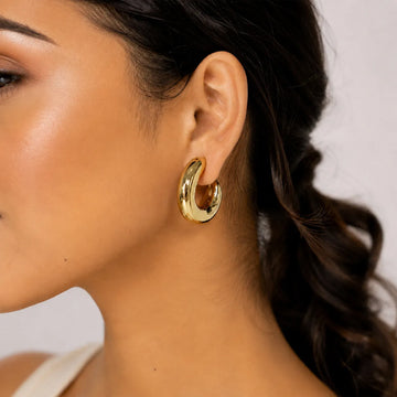 Close-up of a woman wearing a gold hoop earring with a neutral background
