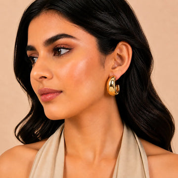 Woman wearing gold hoop earrings against a beige background