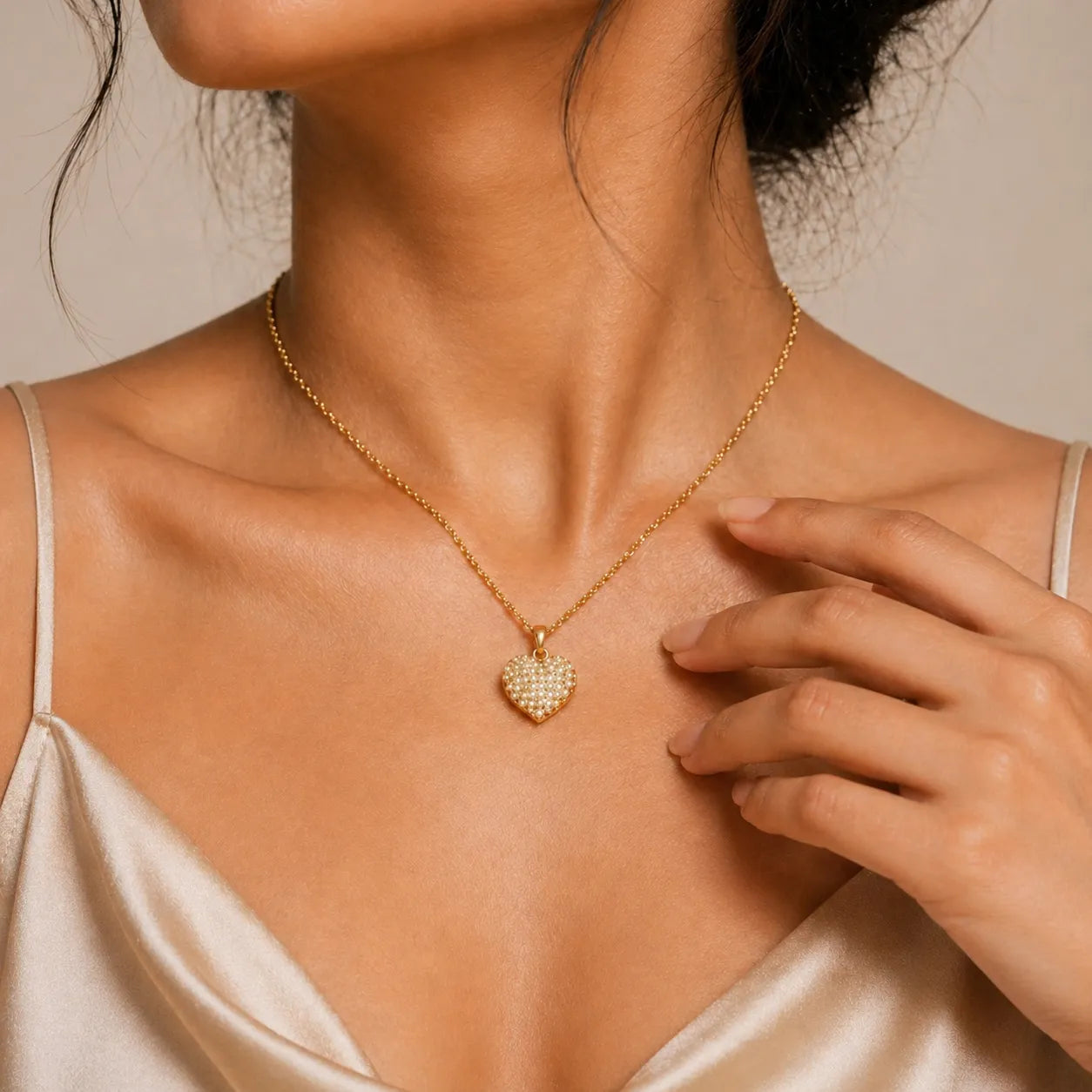Woman wearing a gold necklace with a heart-shaped pendant on a neutral background