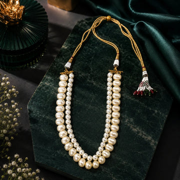 Pearl necklace with tassels on a dark green stone surface