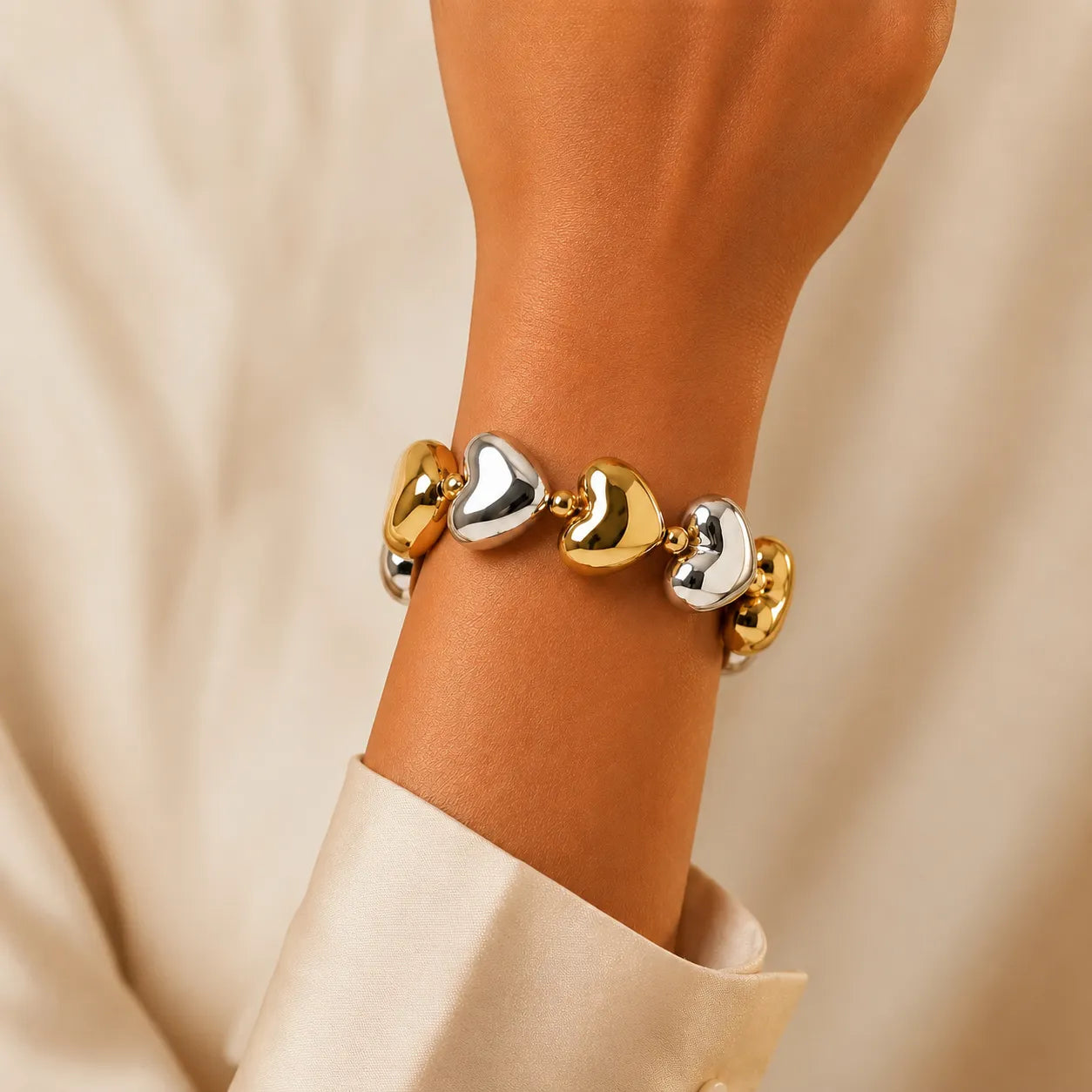 Gold and silver heart-shaped bracelet on a wrist against a beige background