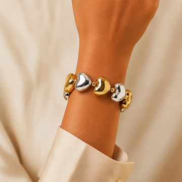 Gold and silver heart-shaped bracelet on a wrist against a beige background
