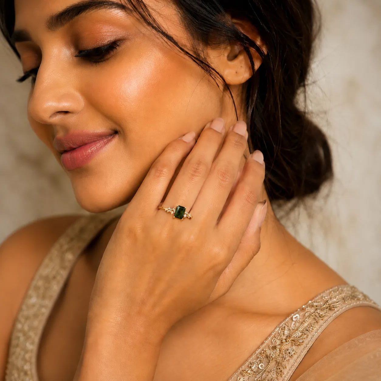 Woman wearing a gold ring with a green gemstone, close-up of face and hand.
