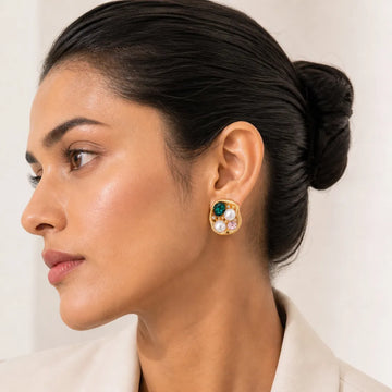 Woman wearing a gold earring with colored stones against a neutral background