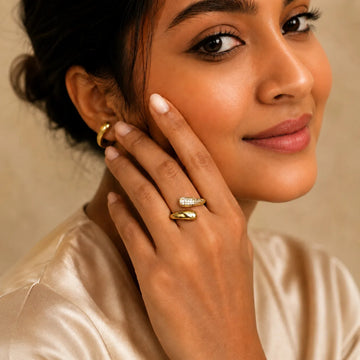Woman wearing gold earrings and ring against a beige background